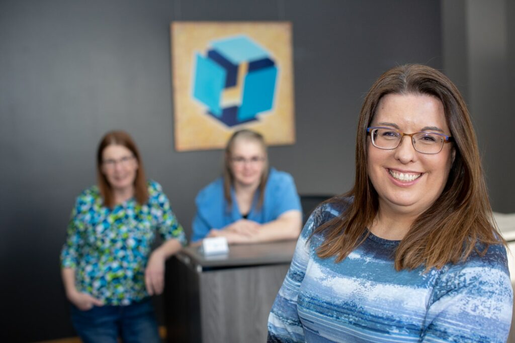 3 women standing in a professional office setting smiling at the camera